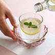 Hand pouring liquid into a glass with lemon and mint on a light pink background