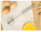Handheld egg beater with eggs and a bowl of whisked eggs on a wooden surface