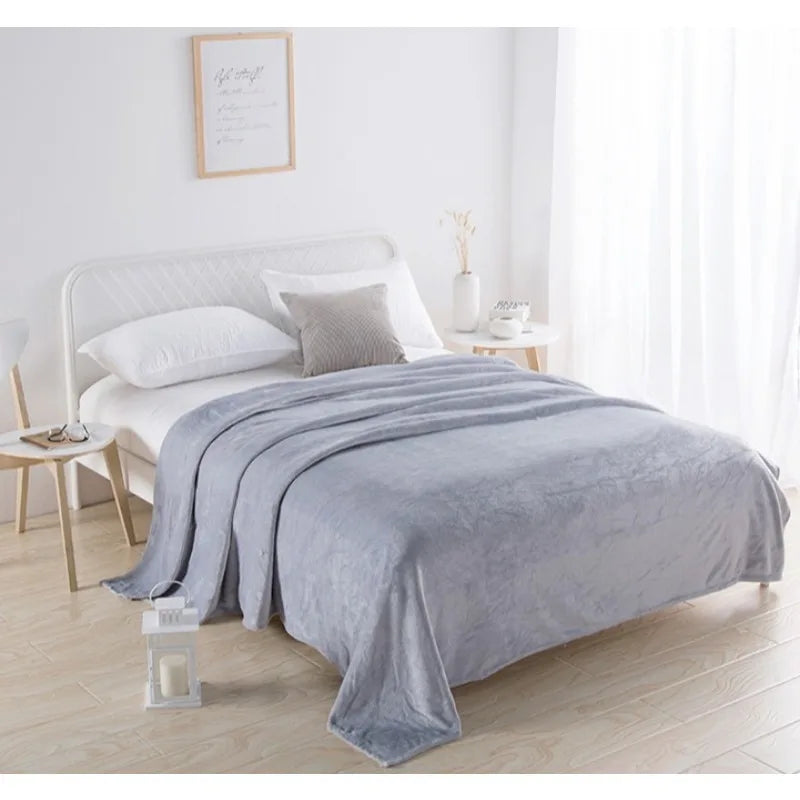 Gray blanket on a bed in a bright bedroom with white walls and wooden floors.
