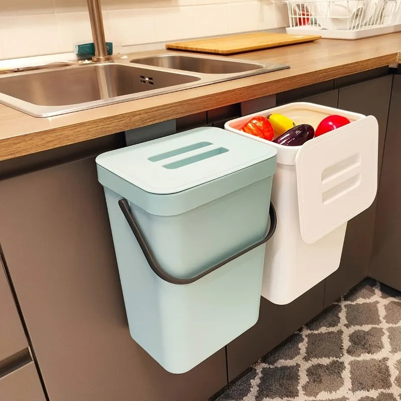 Kitchen compost bin with a lid and another bin with colorful vegetables on a kitchen counter.