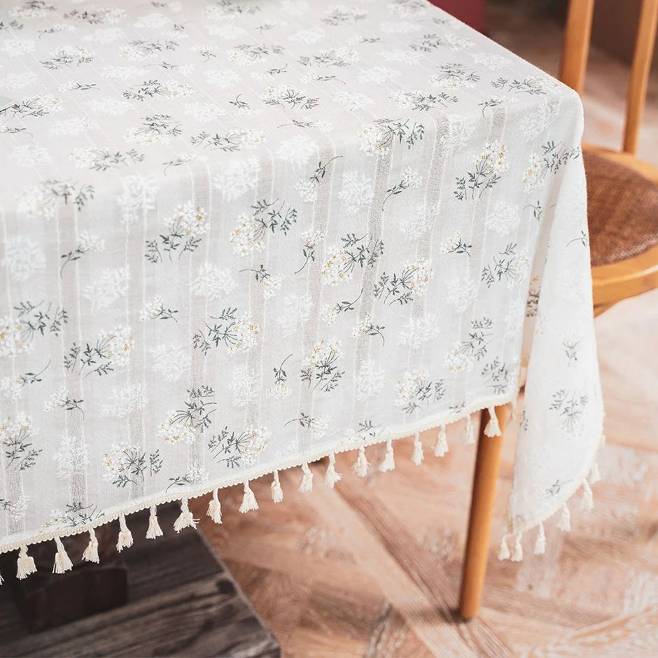 Floral patterned tablecloth with tassels on a wooden table.