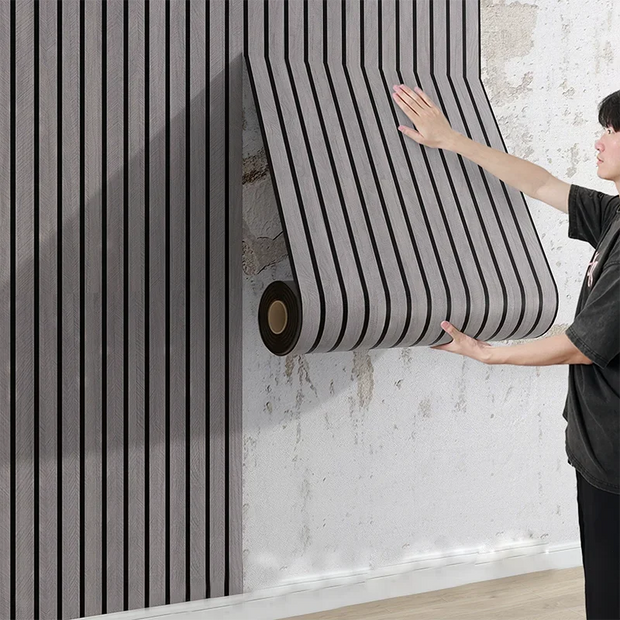 Person holding a large roll of black and gray striped wallpaper against a textured wall.