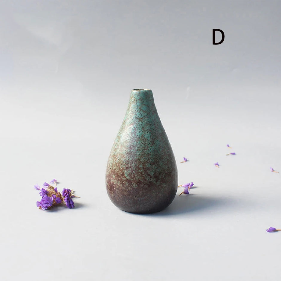 Textured ceramic vase on a light gray background with scattered purple flowers.