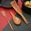 Set of wooden cooking utensils on a red and gray surface with pots and pans in the background.