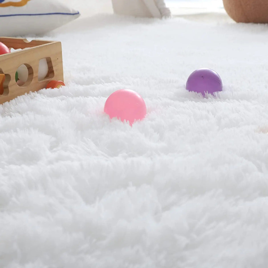 White fluffy rug with pink and purple balls on a light wooden floor.