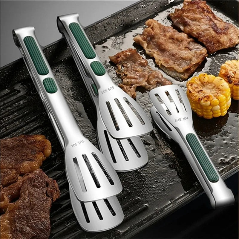 Set of four metal spatulas with green handles on a grill with cooked meat and corn.