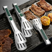Set of four metal spatulas with green handles on a grill with cooked meat and corn.