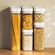 Set of five clear containers with lids, each filled with different types of pasta and beans on a wooden surface.