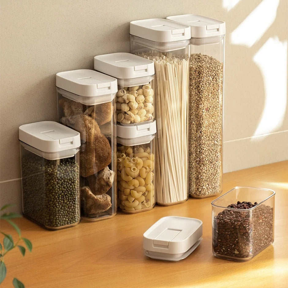 Set of transparent kitchen storage containers with white lids on a wooden surface.