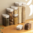 Set of transparent kitchen storage containers with white lids on a wooden surface.