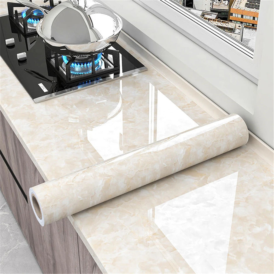 Roll of beige marble-patterned vinyl wrap on a kitchen countertop with a gas stove.