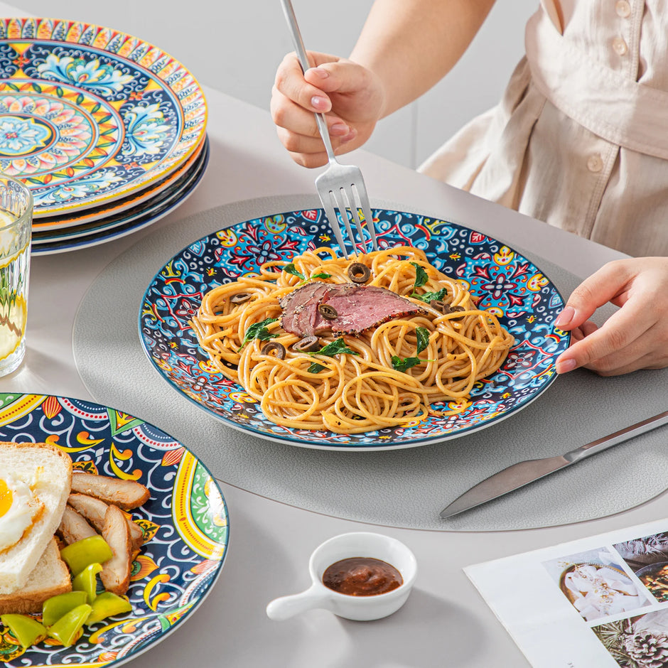 Colorful plates with spaghetti and meat, a fork, knife, and small cup on a table.