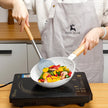 Person cooking colorful vegetables in a white wok on an induction cooktop, wearing a 'Hand Made' apron.