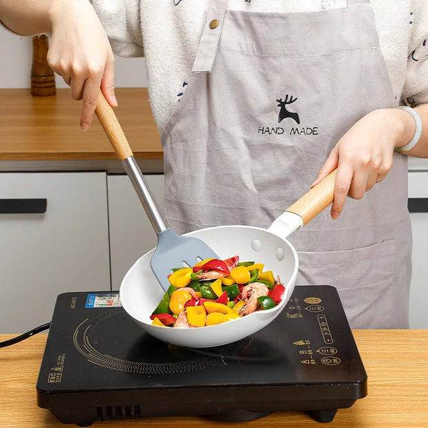 Person cooking colorful vegetables in a white wok on an induction cooktop, wearing a 'Hand Made' apron.