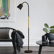 Modern black floor lamp in a living room setting with a chair and table.