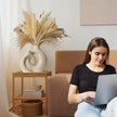 Woman using a laptop on a couch with decorative elements in the background