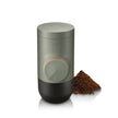 Green coffee grinder with a small pile of ground coffee on a white background