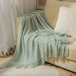 Light green textured throw blanket draped over a beige sofa with white cushions.