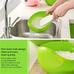 Green colander with rice being washed in a kitchen sink, featuring text about its design.