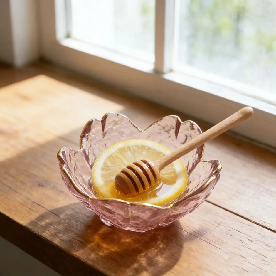 Pink glass bowl with honey, lemon, and a wooden dipper on a wooden surface.