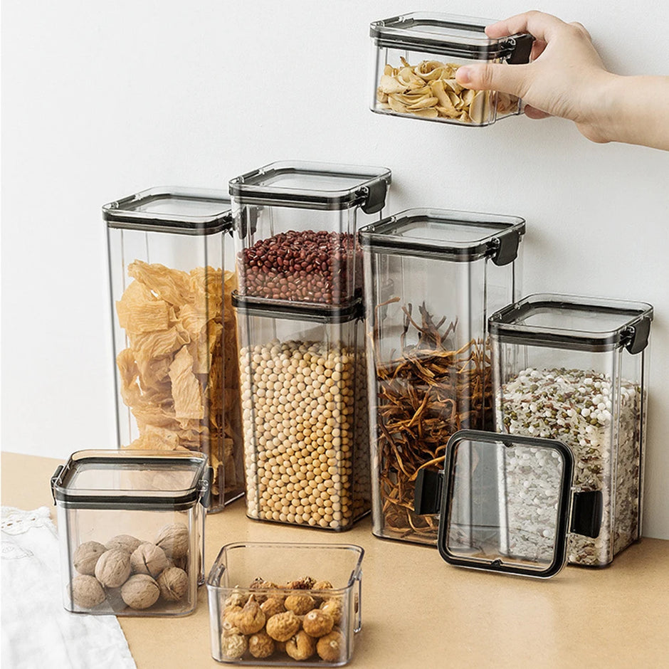 Set of clear storage containers with black lids on a light surface, filled with various food items.