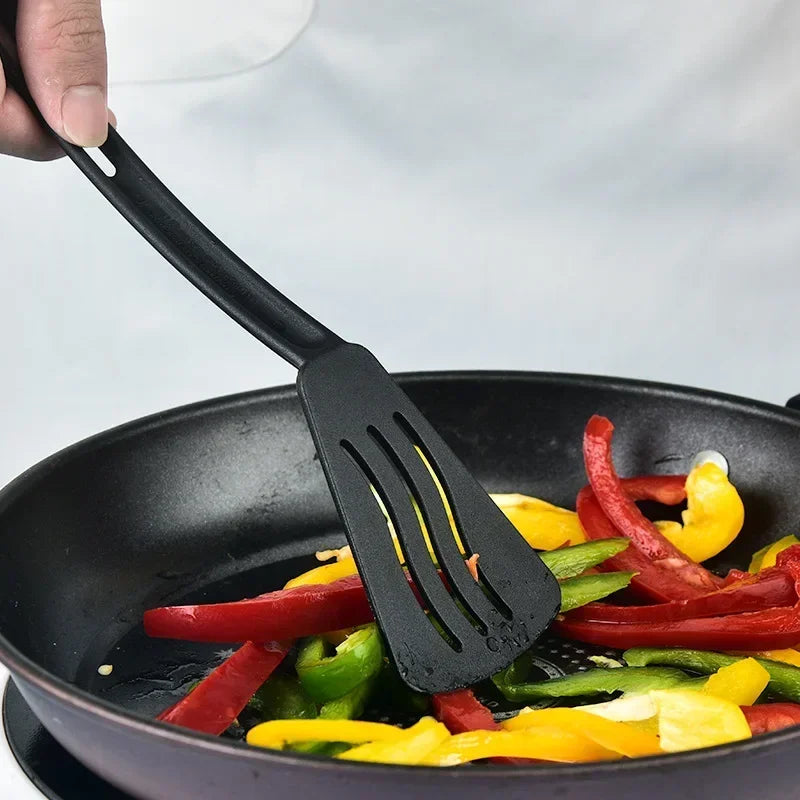 Black slotted spatula stirring colorful bell peppers in a pan.