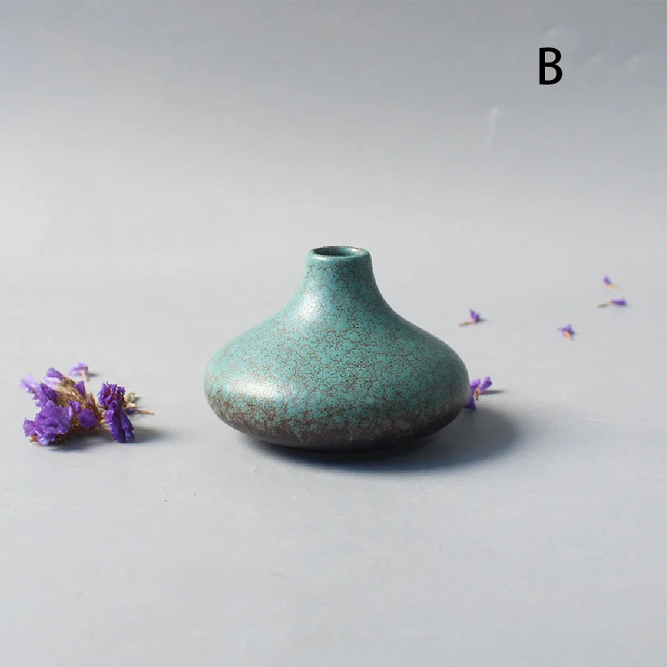 Teal ceramic vase on a light gray background with small purple flowers.