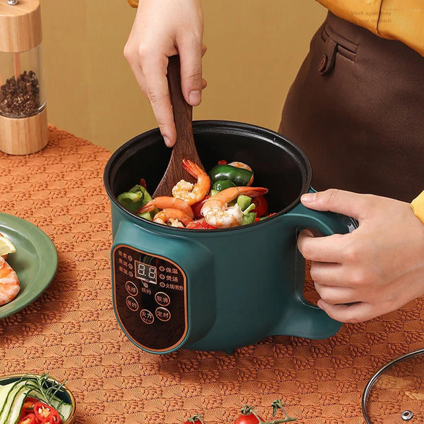 Person cooking in a portable electric pot with vegetables and shrimp on a textured surface.