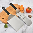 Two metal spatulas on a wooden cutting board with vegetables on a marble background