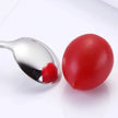 Red cherry tomato next to a silver spoon on a white background