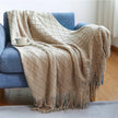 Beige diamond patterned throw blanket draped over a blue sofa with a cup on a small table.