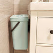 Green trash can attached to a wall in a bathroom setting