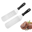 Two metal spatulas with black handles on a white background, accompanied by cooked meat and herbs.