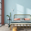 Bedroom with gold metal bed, pink pillows, and a blue textured wall.