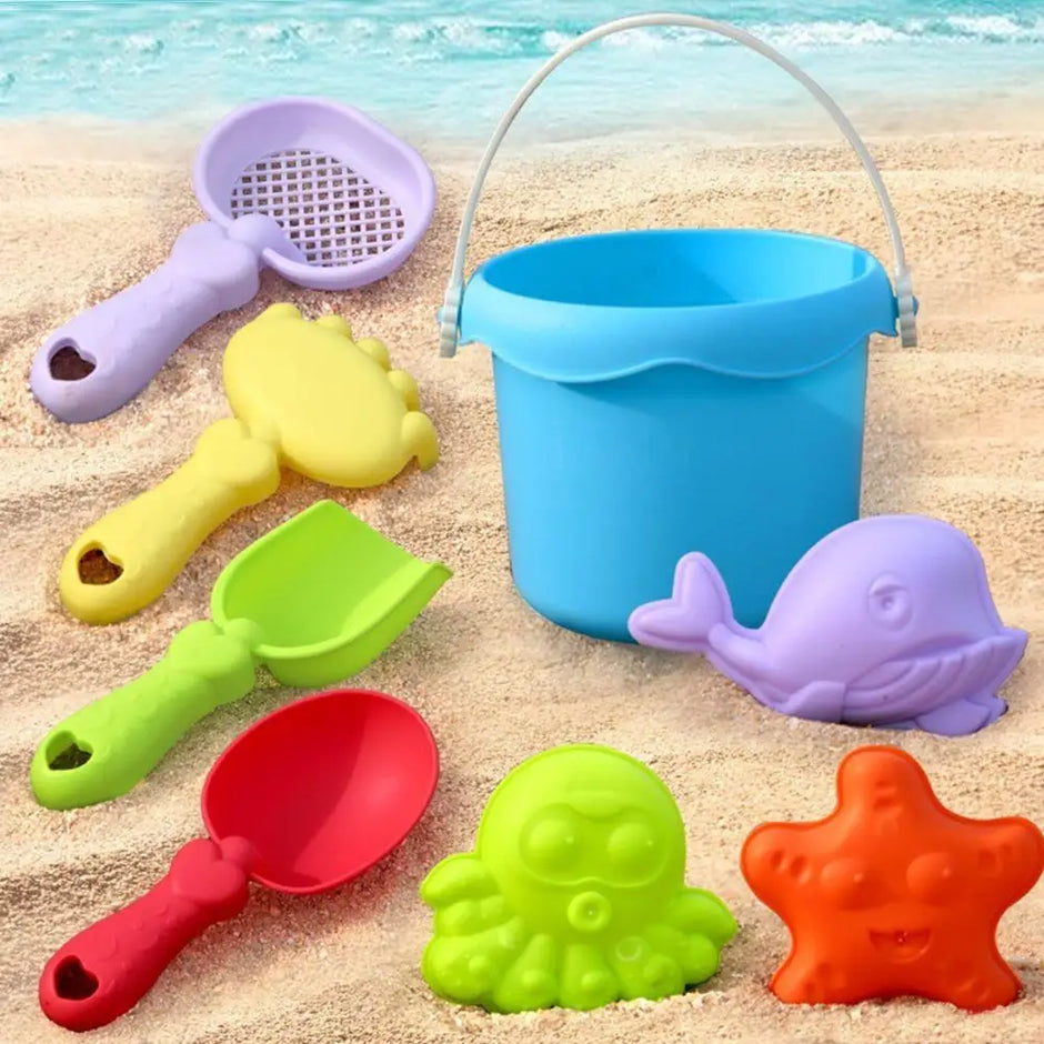 Set of colorful sand toys including a bucket, shovels, and molds on a sandy beach.