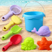 Set of colorful sand toys including a bucket, shovels, and molds on a sandy beach.