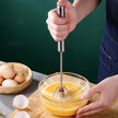 Person whisking eggs in a glass bowl with a hand mixer on a wooden cutting board.