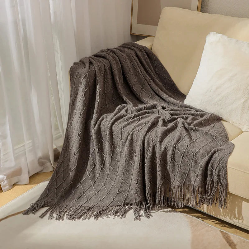 Gray textured throw blanket draped over a beige sofa with white cushions.