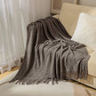 Gray textured throw blanket draped over a beige sofa with white cushions.