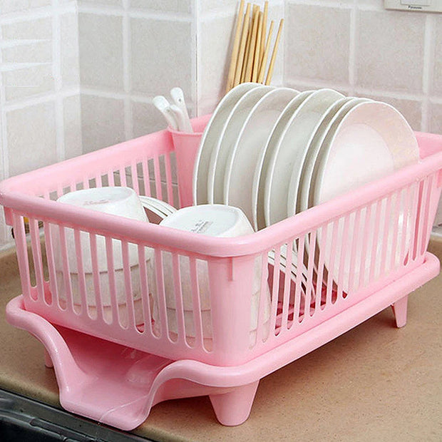 Pink dish drying rack with plates and utensils on a kitchen counter.