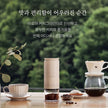 Coffee-making setup with a grinder, coffee beans, and a pot on a table with a blurred green background.