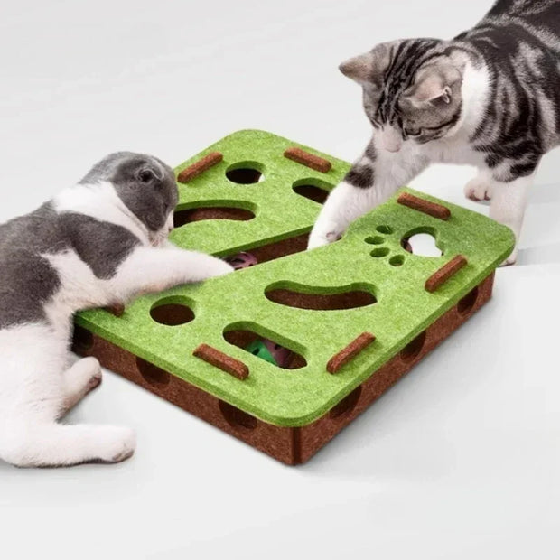 Two cats playing with a green and brown puzzle toy on a white surface