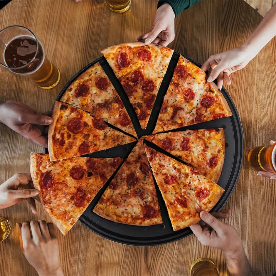 Sliced pizza on a wooden table with people reaching for slices