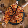 Sliced pizza on a wooden table with people reaching for slices