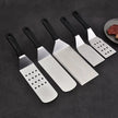 Set of five metal spatulas with black handles on a dark surface.