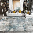 Modern living room with a gray and blue patterned rug, white sofa with colorful pillows, and decorative wall art.