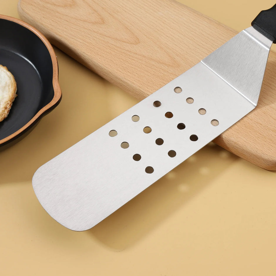 Metal spatula with perforated design on a wooden cutting board and beige surface