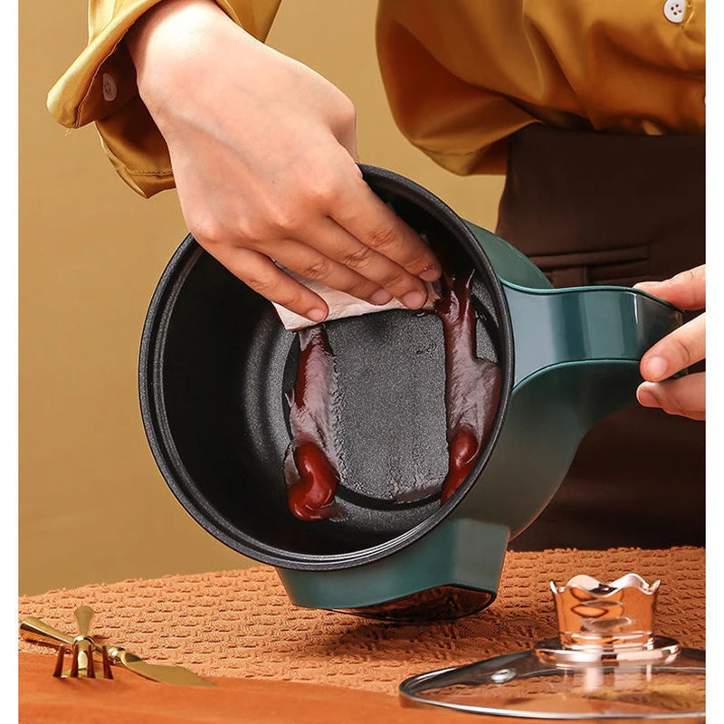 Person cleaning a green pot with a black interior on a wooden surface.