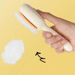 Hand holding a white grooming brush with a yellow background