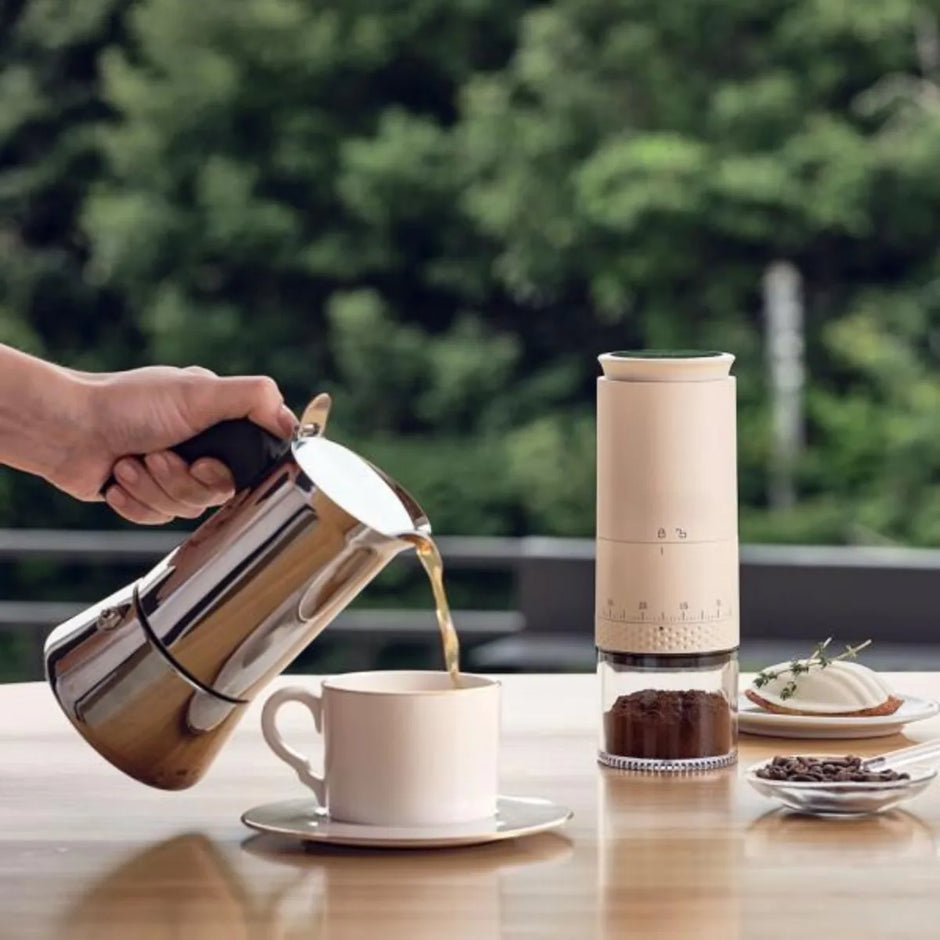 Person pouring coffee from a French press into a cup on a wooden table with a blurred green outdoor background.